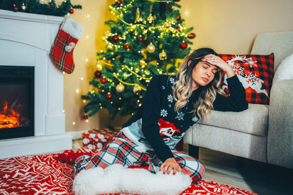 Young woman sitting near Christmas tree reflecting on unexpected pregnant situation.